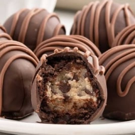 A plate full of chocolate chip cookie dough brownie bombs, with one bomb sliced open to showcase the gooey cookie dough and chocolate chip filling.