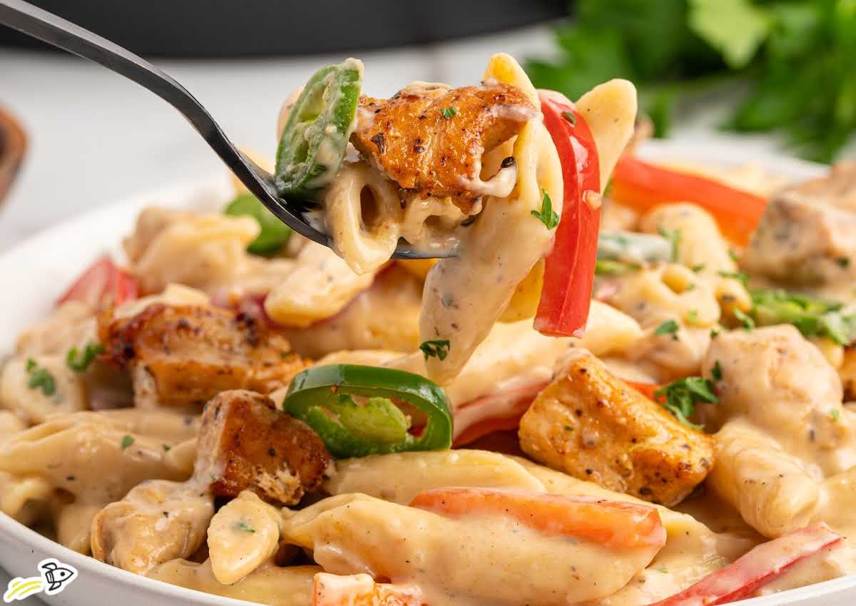 fork lifting creamy rattlesnake pasta with chicken, penne, jalape&ntilde;os, and red bell peppers
