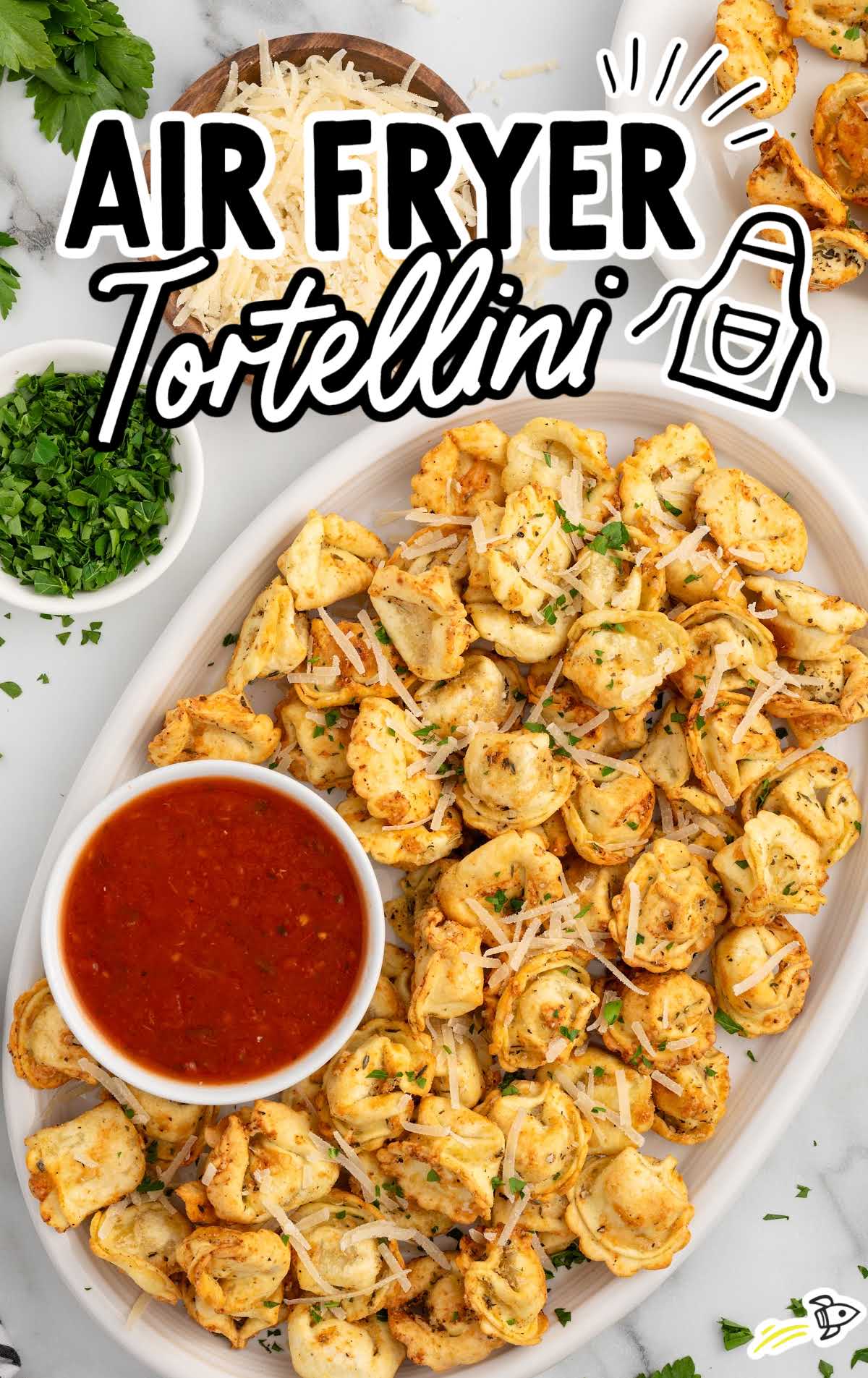 A close-up of air fryer tortellini on a platter, golden brown and topped with Parmesan cheese and parsley, next to a bowl of marinara sauce.