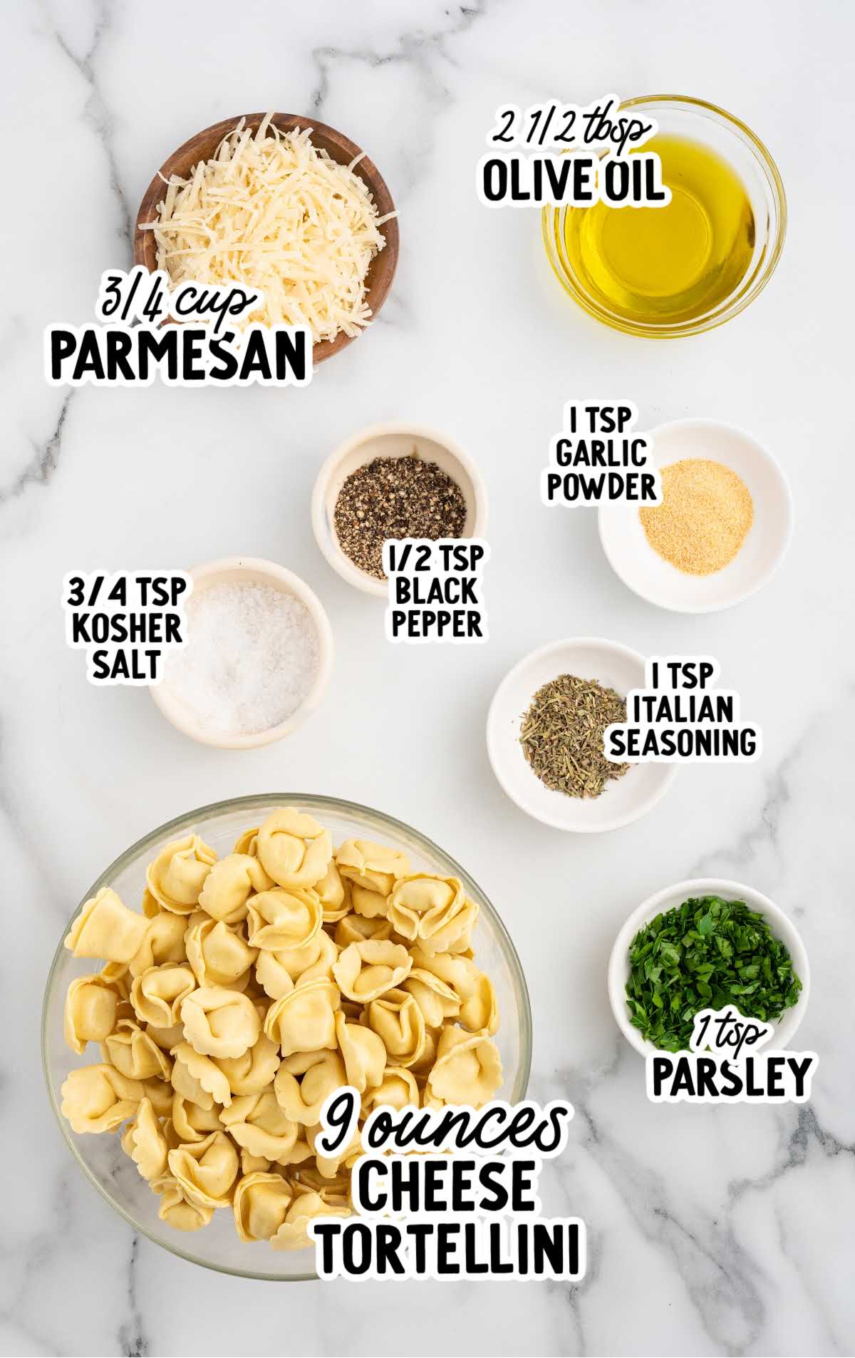 Ingredients for air fryer tortellini, including cheese tortellini, olive oil, Parmesan cheese, Italian seasoning, garlic powder, parsley, salt, and black pepper, displayed on a marble surface.