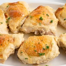 Plate of golden-brown Amish chicken thighs baked in a creamy sauce and topped with chopped parsley.