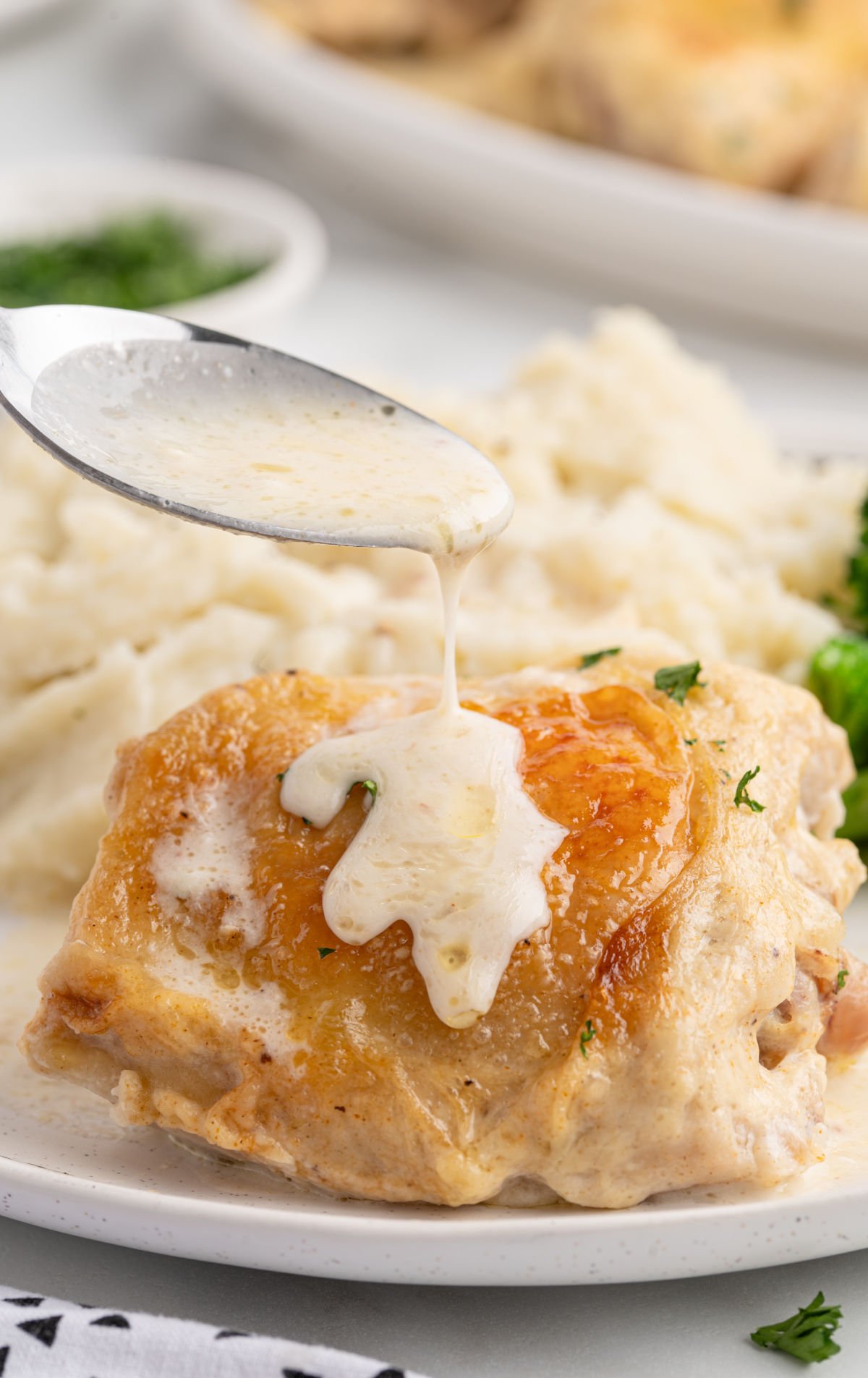 ChatGPT said:
Close-up of creamy gravy being spooned over a golden-brown baked chicken thigh, served on a white plate with mashed potatoes and broccoli in the background.