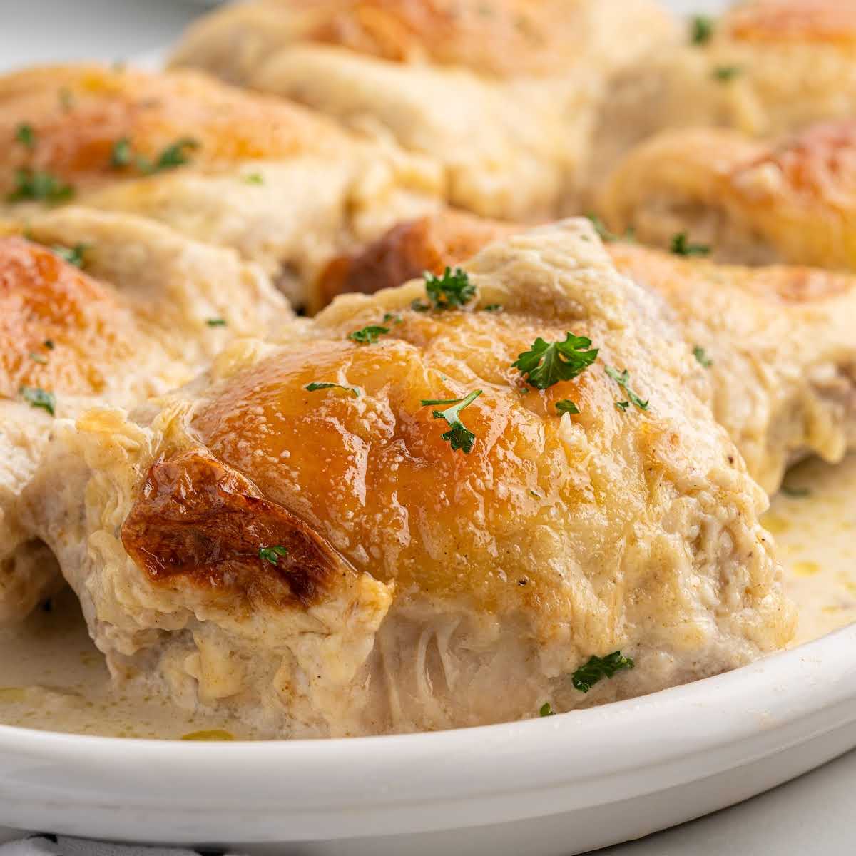 Side view of tender Amish chicken thighs in a creamy sauce on a white plate, garnished with parsley.