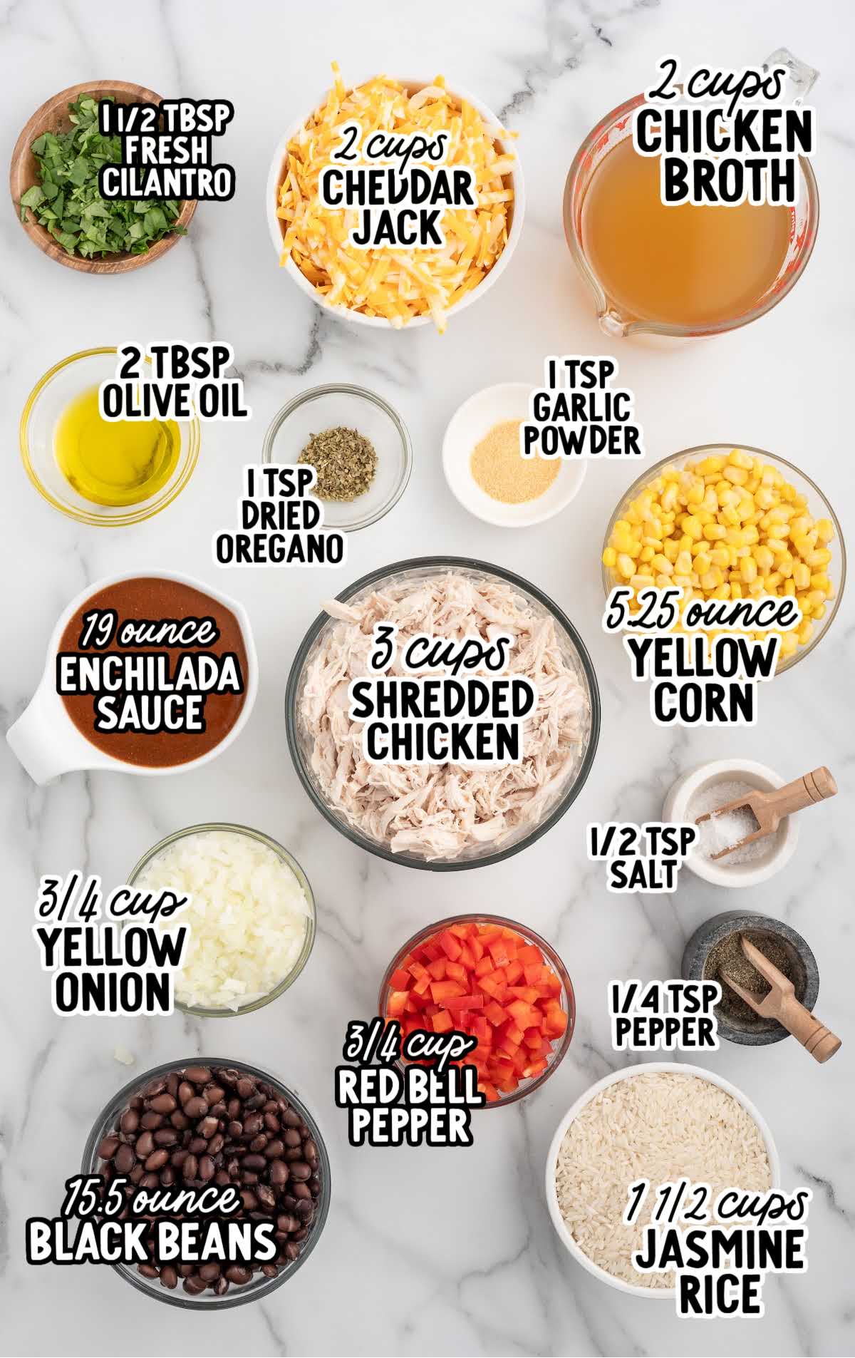 A flat lay of the ingredients for chicken enchilada rice casserole, including shredded chicken, jasmine rice, enchilada sauce, cheddar jack cheese, black beans, corn, and various seasonings, neatly arranged on a white marble surface.