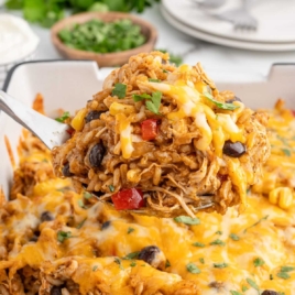 A perfectly portioned scoop of chicken enchilada rice casserole lifted from the baking dish, with melted cheese and colorful ingredients visible, perfect for a recipe card.