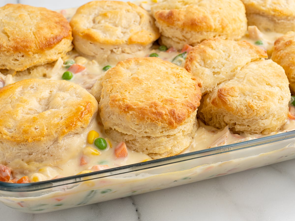 A glass baking dish filled with creamy Chicken Pot Pie Casserole, topped with golden-brown biscuits and packed with mixed vegetables like carrots, peas, and corn in a rich sauce.