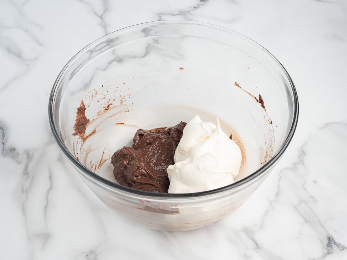 A clear glass bowl with chocolate mixture and a dollop of whipped cream on a marble countertop, perfect for assembling your favorite Chocolate Pudding Pie.