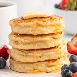 fluffy pancakes stacked on top of each other and topped with a slice of butter and syrup on a plate with fruit