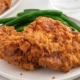 Juicy fried pork chop cut in half to show the tender inside, served with green beans.
