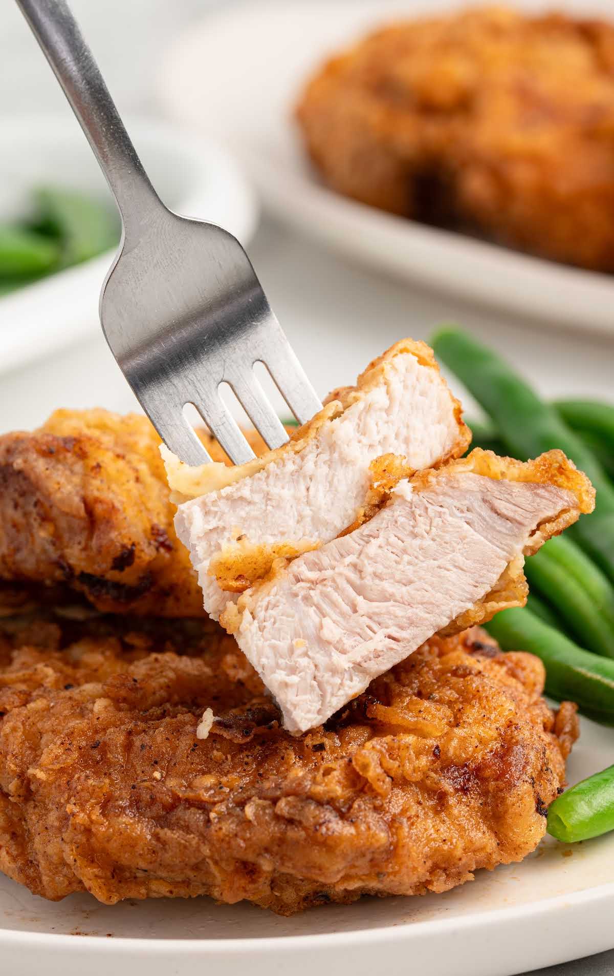 Fork holding a sliced piece of juicy fried pork chop over a plate.