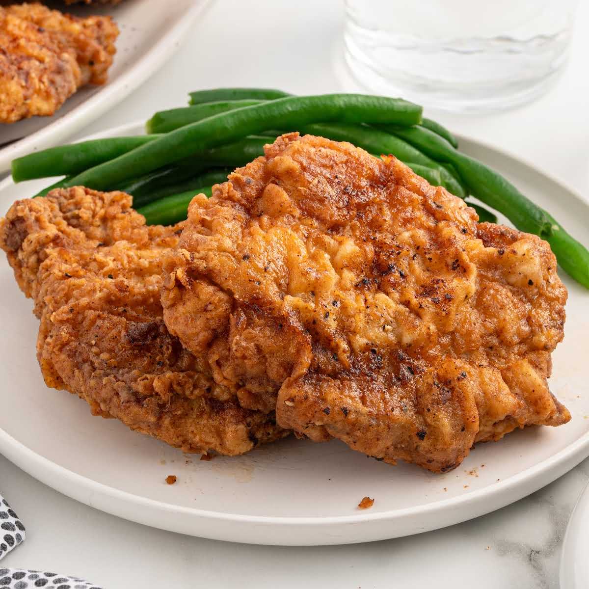 Plate of two fried pork chops with green beans on the side, ready to serve.