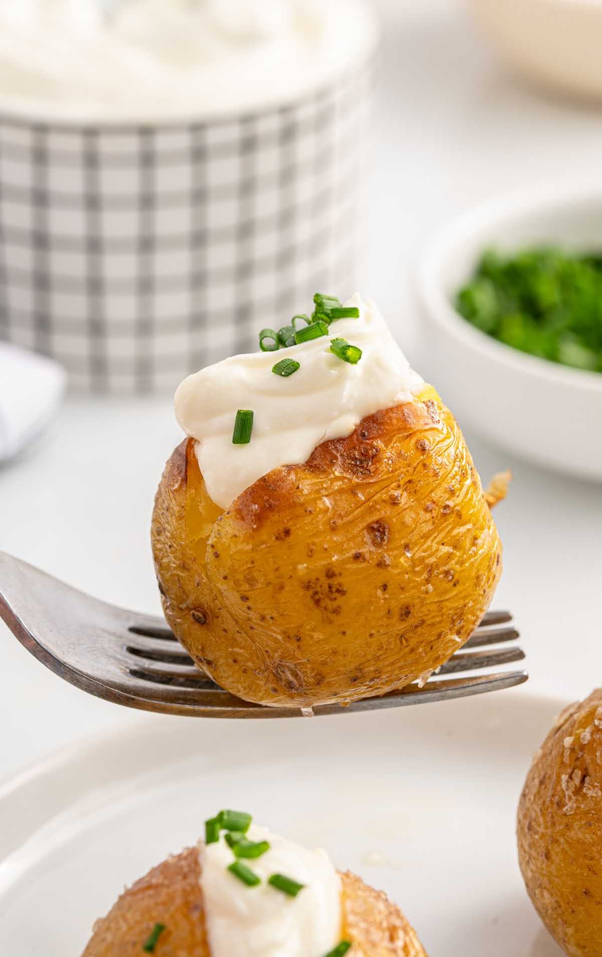 a mini baked potato topped with sour cream and chives on a fork