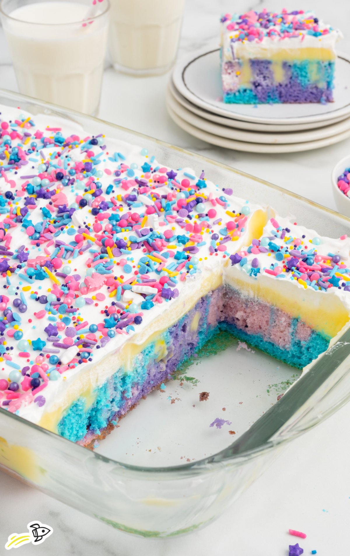 A unicorn poke cake in a glass baking dish with a few pieces taken out of it. 