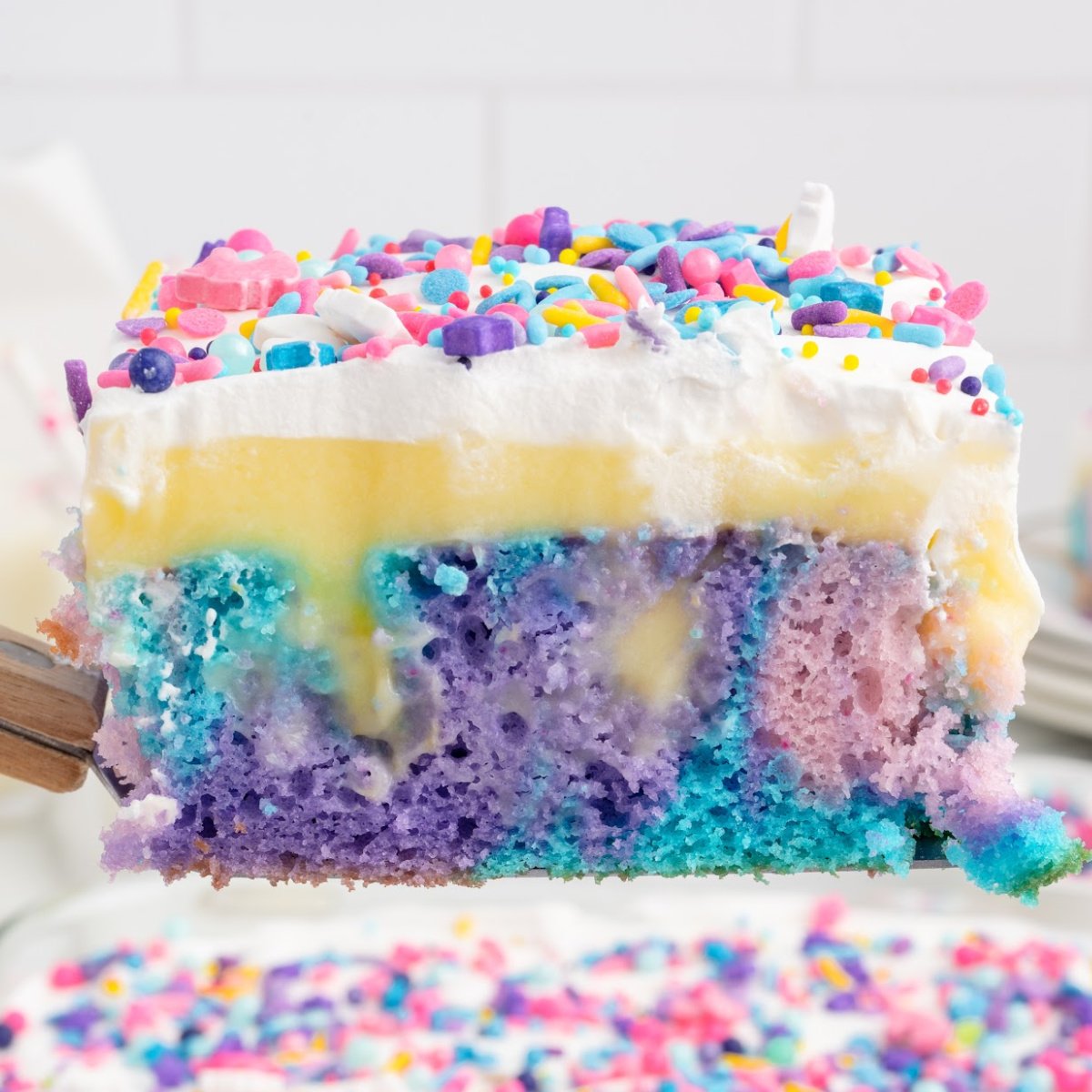 A slice of unicorn poke cake is lifted from a cake. You can see all the layers.