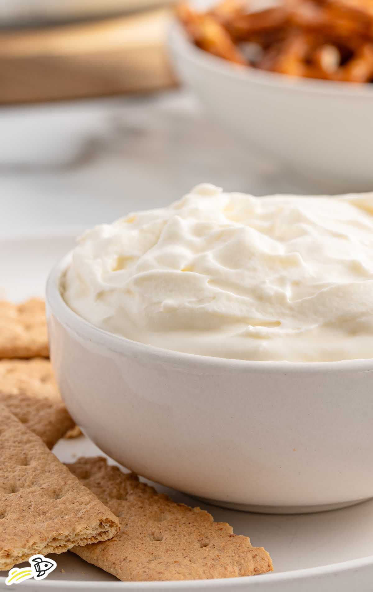 A close-up of a graham cracker scooping out the cherry-topped cheesecake dip from the bowl, showcasing the layers.