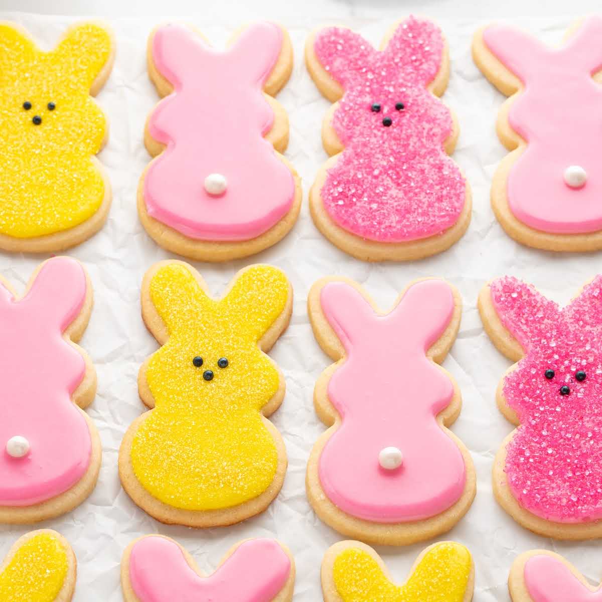 Decorated Easter bunny sugar cookies with pink and yellow icing arranged in rows on parchment paper
