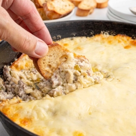 A golden-brown Philly cheesesteak dip in a skillet, served with toasted bread slices.