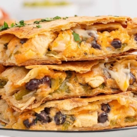 Stacked slices of chicken sheet pan quesadillas filled with cheese, black beans, and green peppers, displayed on a plate.