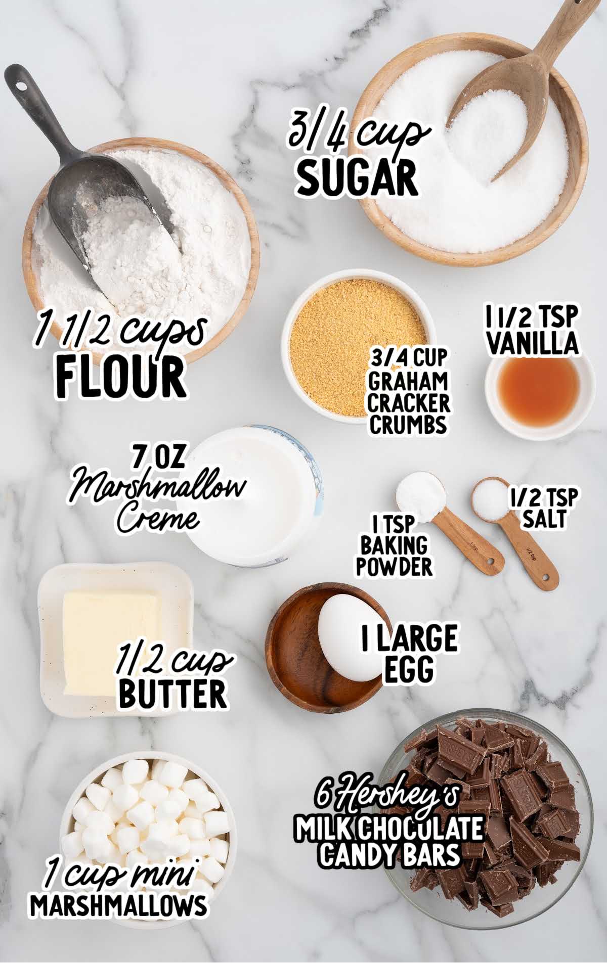 Ingredients for s'mores pie laid out on a marble surface, including graham cracker crumbs, mini marshmallows, chocolate, butter, sugar, and flour.