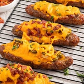 Overhead view of cheesy sausage popper boats on a wire rack with bowls of chopped parsley, shredded cheese, and bacon bits nearby.