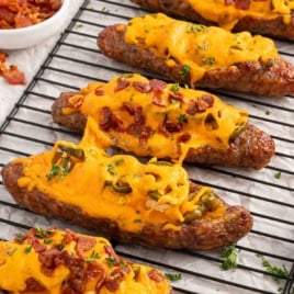 Baked sausage popper boats on a cooling rack, loaded with cheddar cheese, jalapeños, and chopped bacon, garnished with parsley.