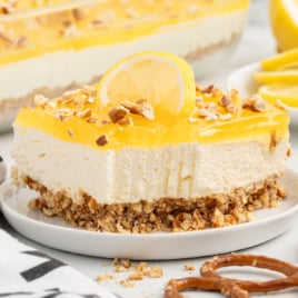 A slice of lemon pretzel salad is on a white plate with a bite missing from it.