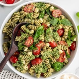 Overhead image of completed pesto pasta salad with rotini, mozzarella, spinach, and cherry tomatoes in a large white bowl.