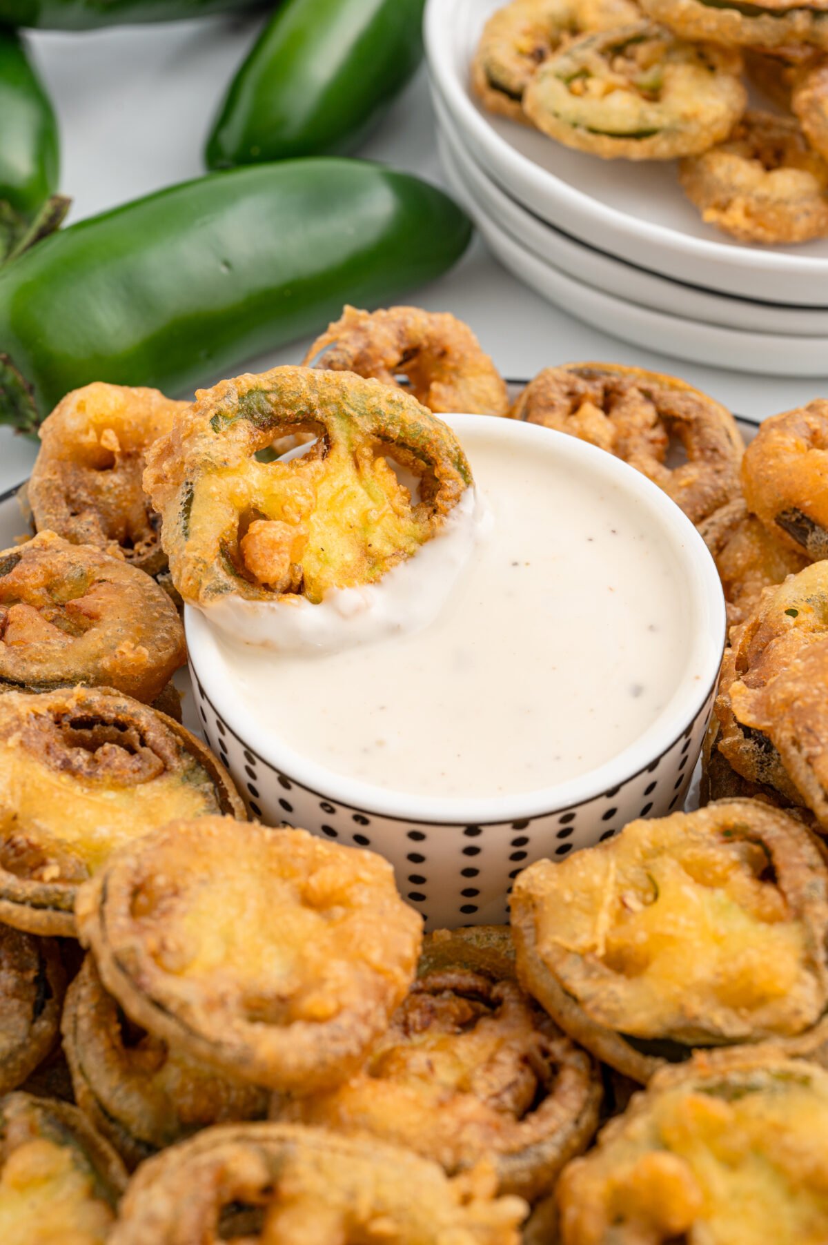 Plate of fried jalapeño bottle caps served with a bowl of ranch dressing and fresh jalapeños on the side