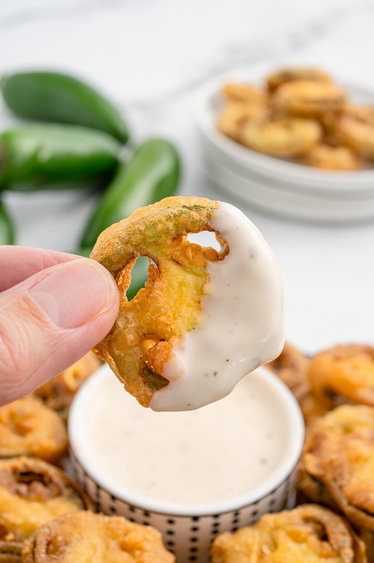 Plate of fried jalapeño bottle caps served with a bowl of ranch dressing and fresh jalapeños on the side