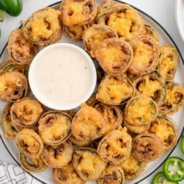 Plate of fried jalapeño bottle caps served with a bowl of ranch dressing and fresh jalapeños on the side