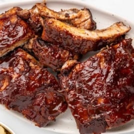 Slow cooker baby back ribs coated in barbecue sauce and served on a platter with extra sauce on the side