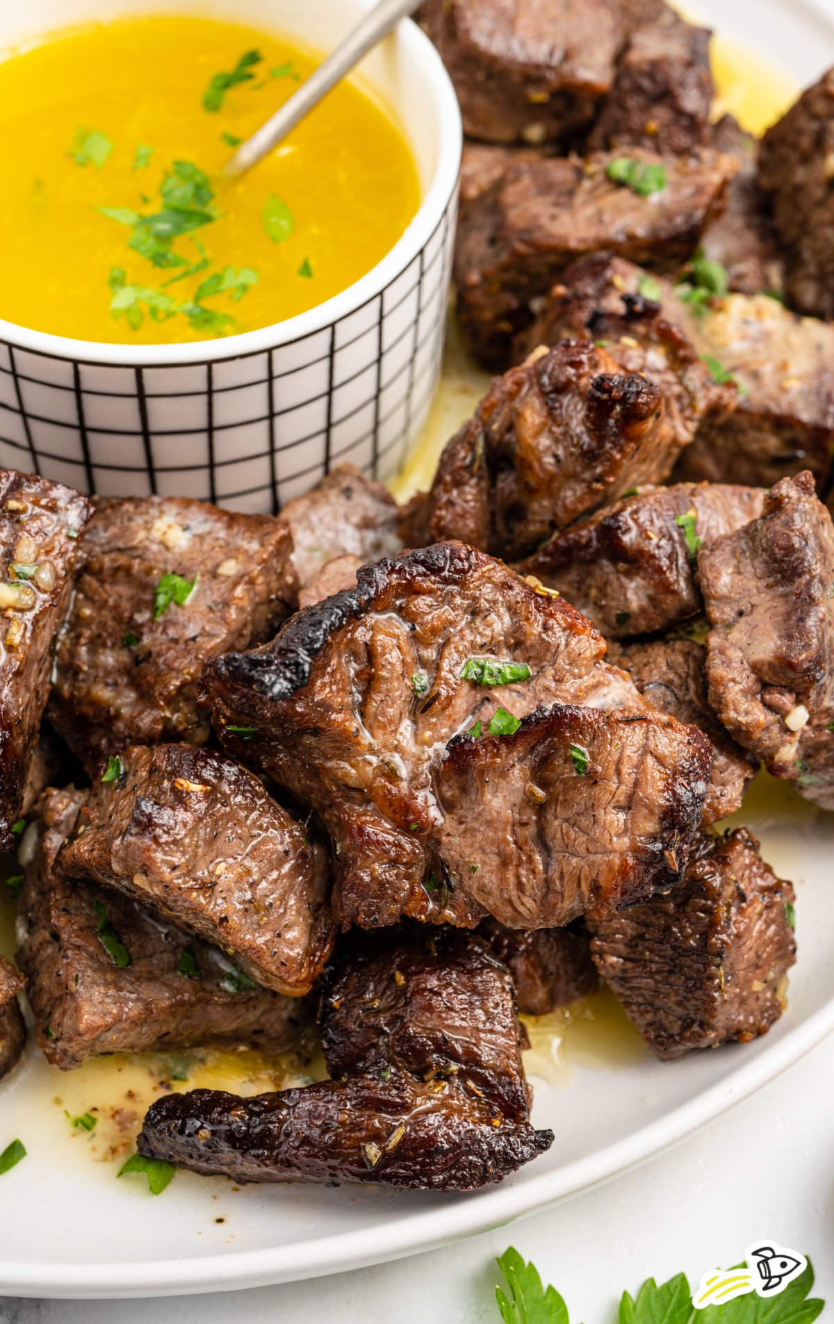 a platter of steak bites with a bowl of melted butter sauce and parsley garnish