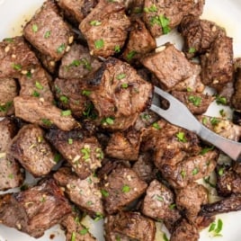 Close-up of juicy steak bites cooked in the air fryer, served with fresh herbs on a white plate