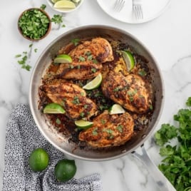 Square image of grilled cilantro lime chicken breasts in a skillet, surrounded by lime wedges and fresh cilantro.