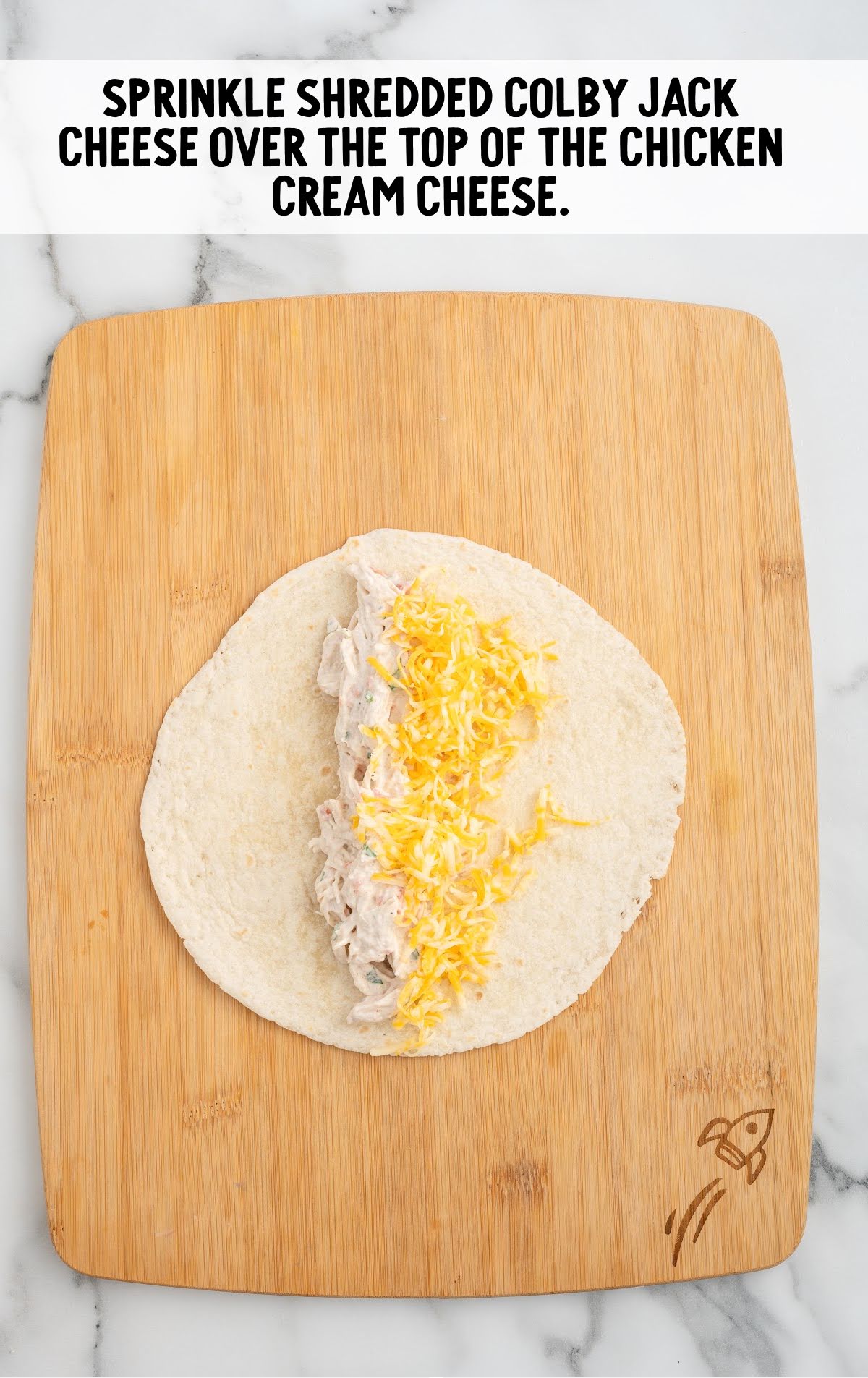 shredded colby jack cheese sprinkled on top of the chicken cream cheese on a tortilla