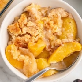Top-down view of a bowl of peach dump cake served with coffee, next to the baking dish.