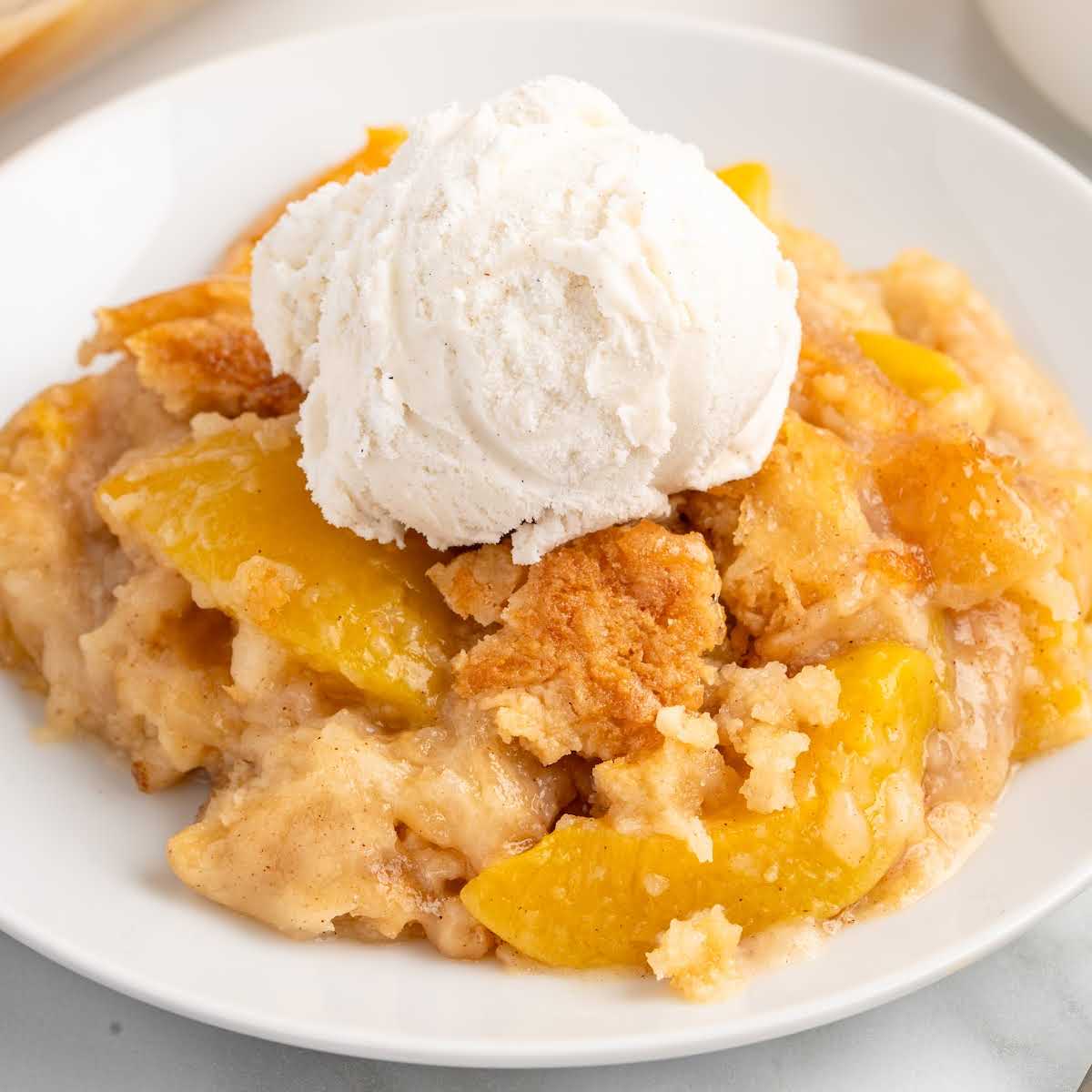 Single serving of peach dump cake on a white plate topped with a scoop of vanilla ice cream.