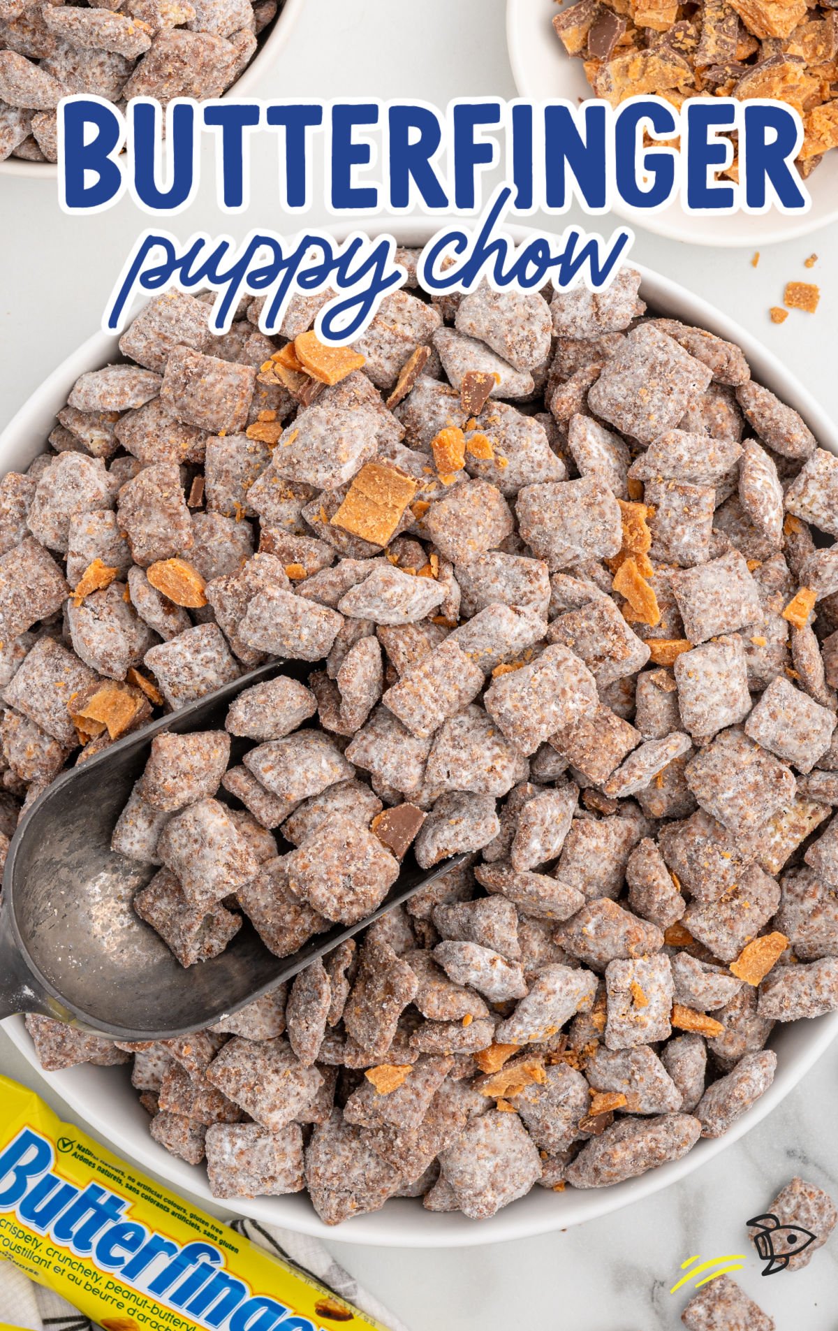 Close-up of a bowl filled with no-bake Butterfinger muddy buddies, dusted with powdered sugar and topped with crushed Butterfinger pieces.