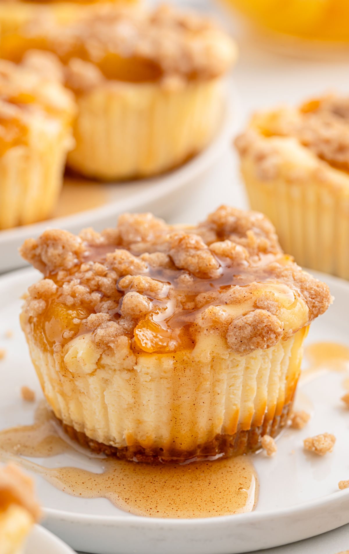 Mini peach cobbler cheesecake topped with cinnamon crumble and drizzled syrup on a white plate.