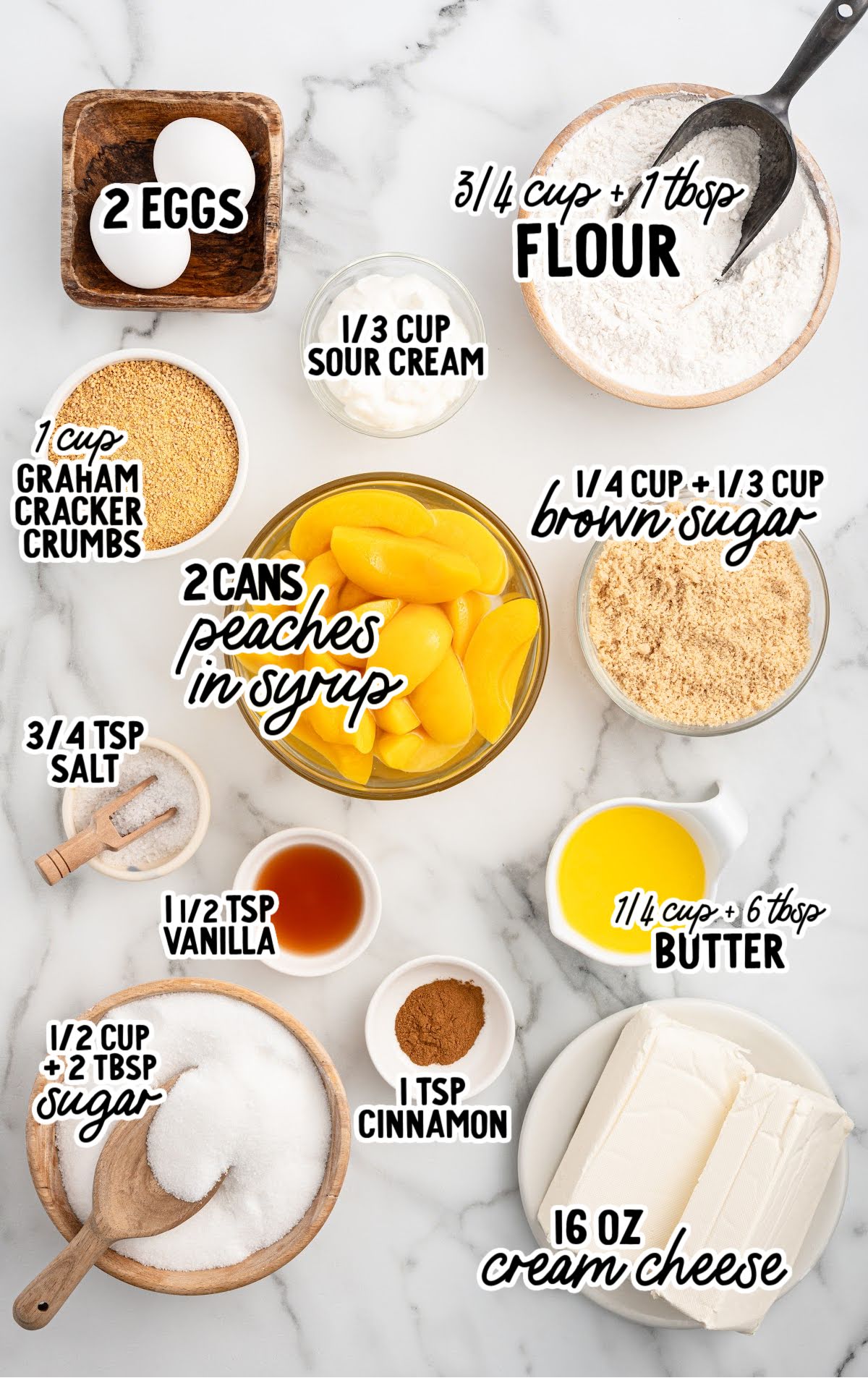 Labeled ingredients for mini peach cobbler cheesecakes displayed on a marble surface, including cream cheese, peaches in syrup, sugar, eggs, flour, cinnamon, butter, vanilla, and graham cracker crumbs.