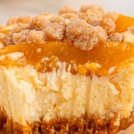 Zoomed-in view of a single peach cobbler cheesecake showing the crumb topping and juicy peaches over a rich cheesecake base, labeled with text for Pinterest.