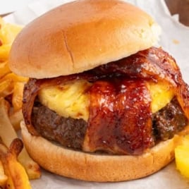 Pineapple bacon burger served with golden French fries and fresh pineapple rings on parchment paper.