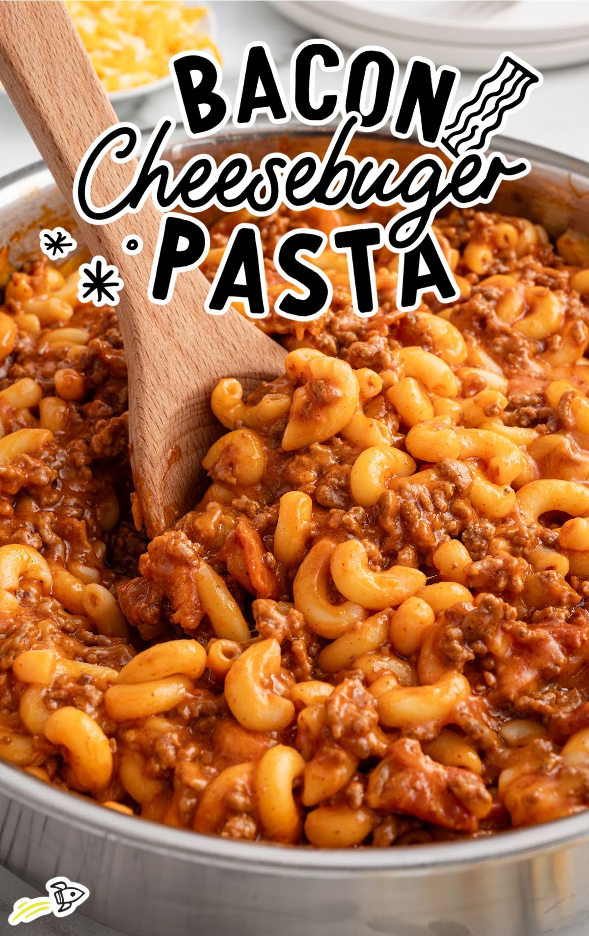 Bacon cheeseburger pasta stirred in a stainless steel skillet with a wooden spoon.