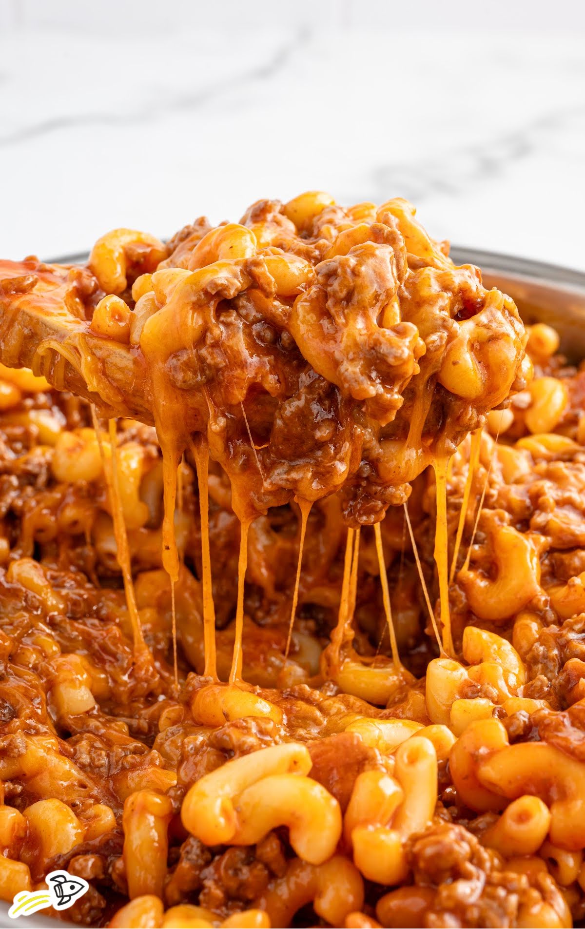 Close-up of gooey bacon cheeseburger pasta lifted from a skillet with melted cheese stretching.