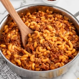 Bacon cheeseburger pasta stirred in a stainless steel skillet with a wooden spoon.