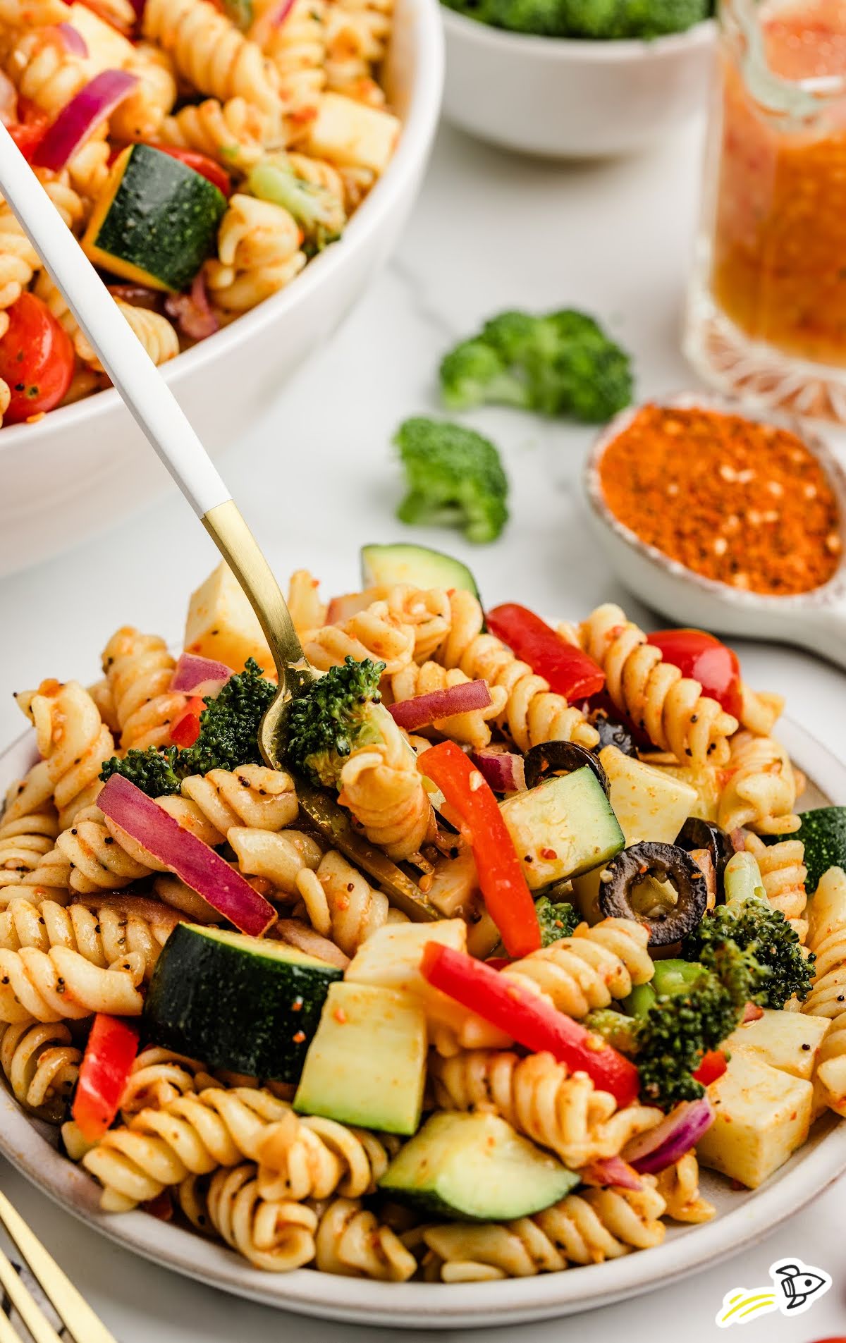 Fork lifting a bite of salad supreme pasta salad from a plate filled with veggies, pasta, and dressing