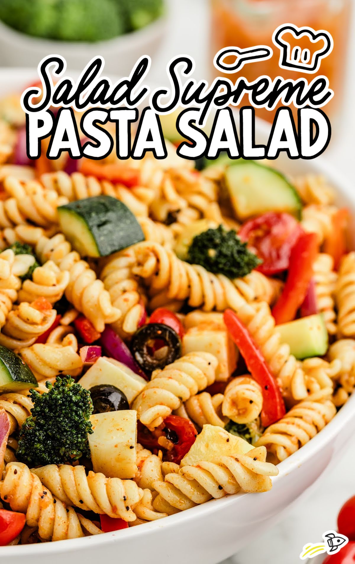 Overhead close-up of salad supreme pasta salad in a white bowl with rotini, zucchini, olives, broccoli, and mozzarella cubes
