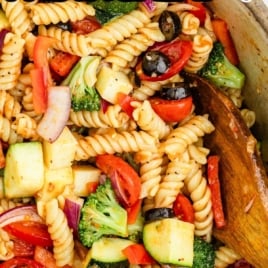 Wooden spoon mixing colorful salad supreme pasta salad with rotini, olives, tomatoes, and red onions in a bowl