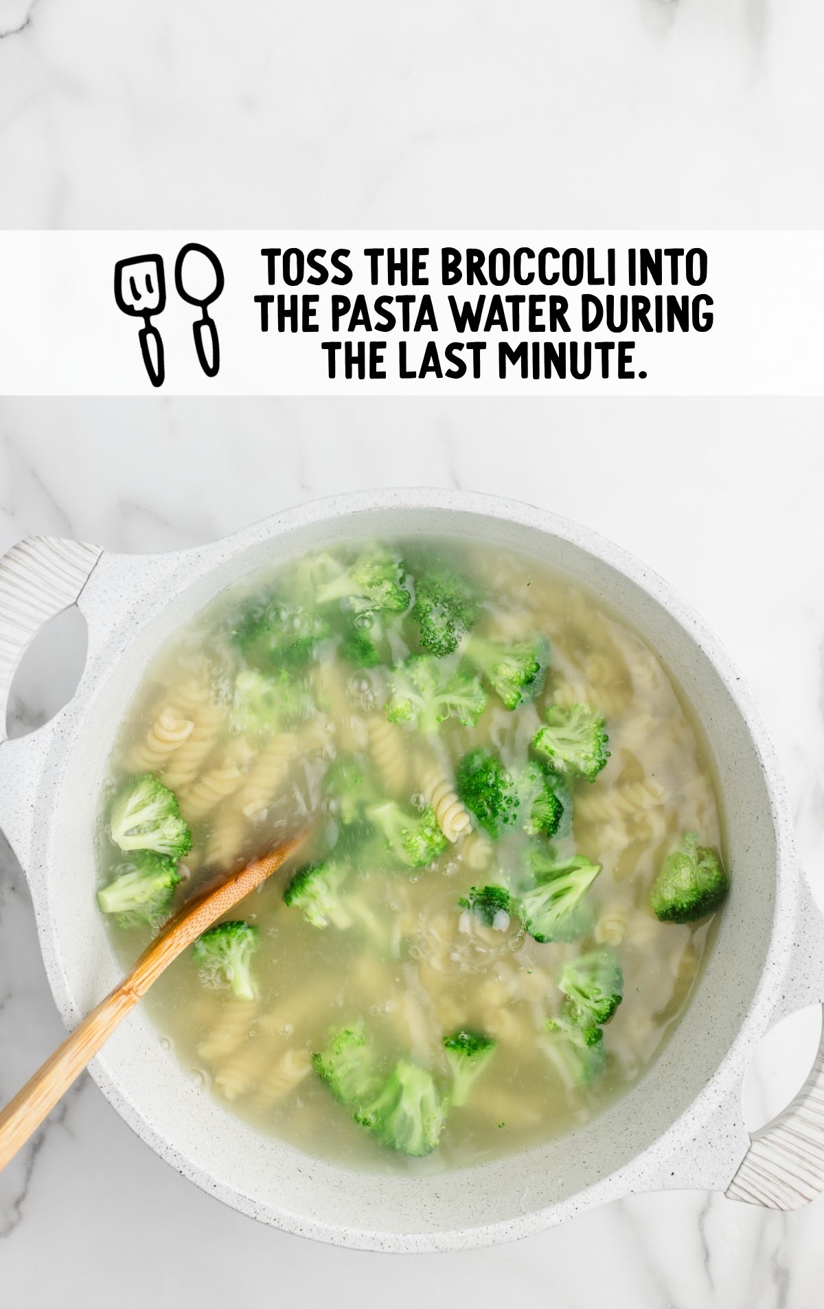 A white pot filled with boiling water, rotini pasta, and broccoli florets on a marble countertop. A wooden spoon is stirring the mixture. Text above the pot reads, "Toss the broccoli into the pasta water during the last minute," with icons of a spatula and spoon.