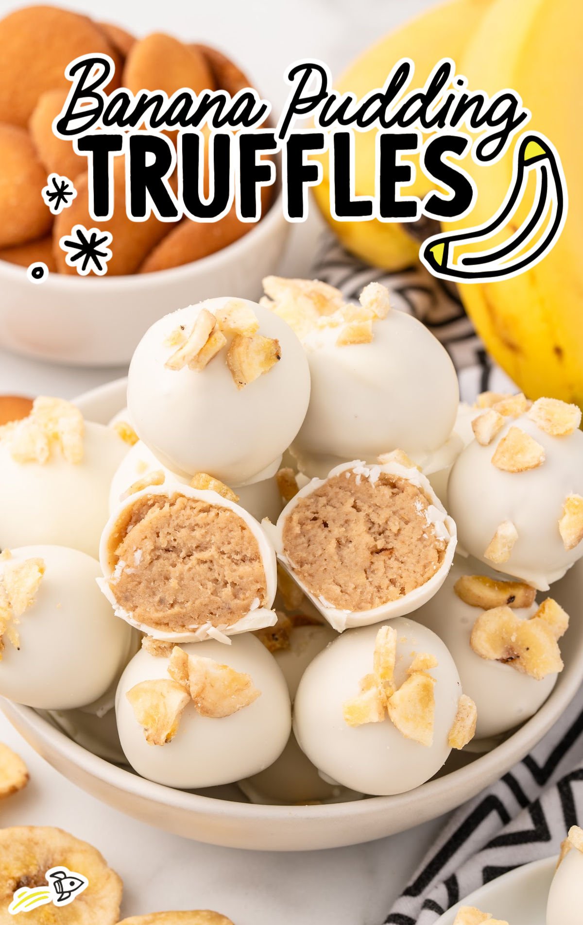 Bowl of banana pudding truffles with two cut open to show soft filling, surrounded by bananas and vanilla wafers, ideal for a recipe card.